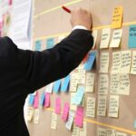Professionnel organisant un atelier Lean Six Sigma avec des post-it sur un tableau pour analyser les processus et identifier des pistes d'amélioration continue.