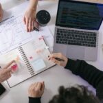 Équipe en réunion de planification autour d'un ordinateur portable, de tableaux de bord et de documents pour coordonner les ventes, la production et la supply chain dans un processus S&OP.
