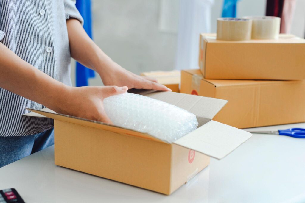 Opérateur préparant une commande e-commerce dans un carton d’expédition avec protection en papier bulle avant l’envoi au client.
